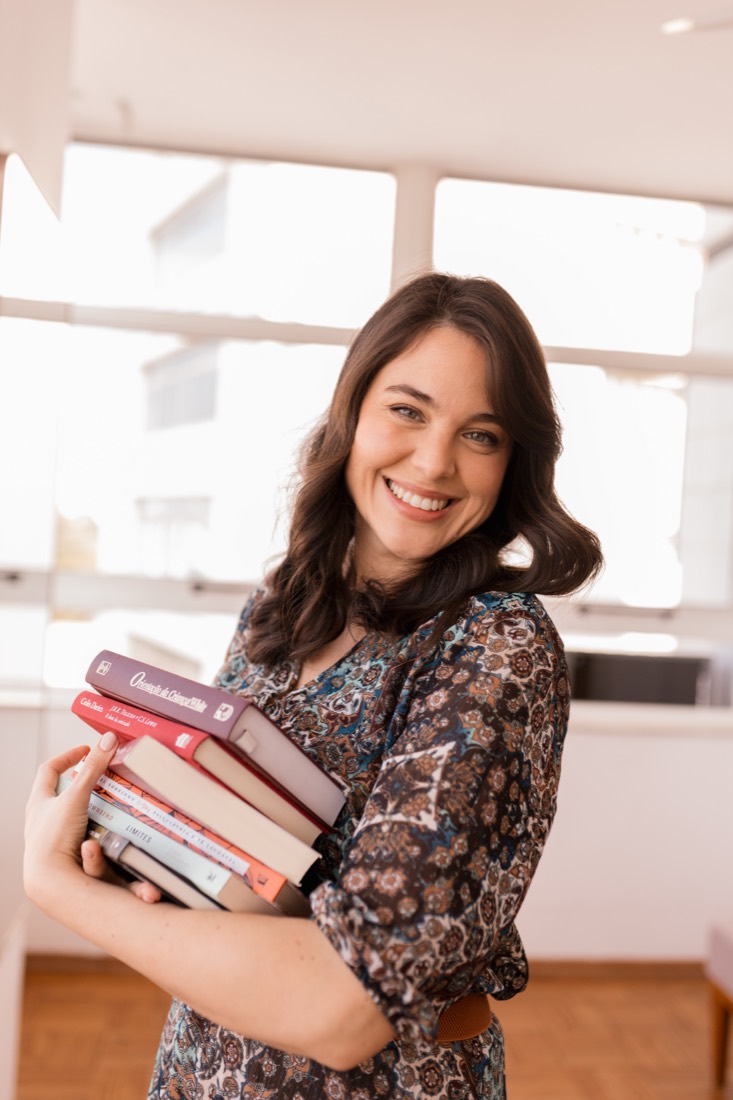 Faíla Thomé segurando uma pilha de livros
